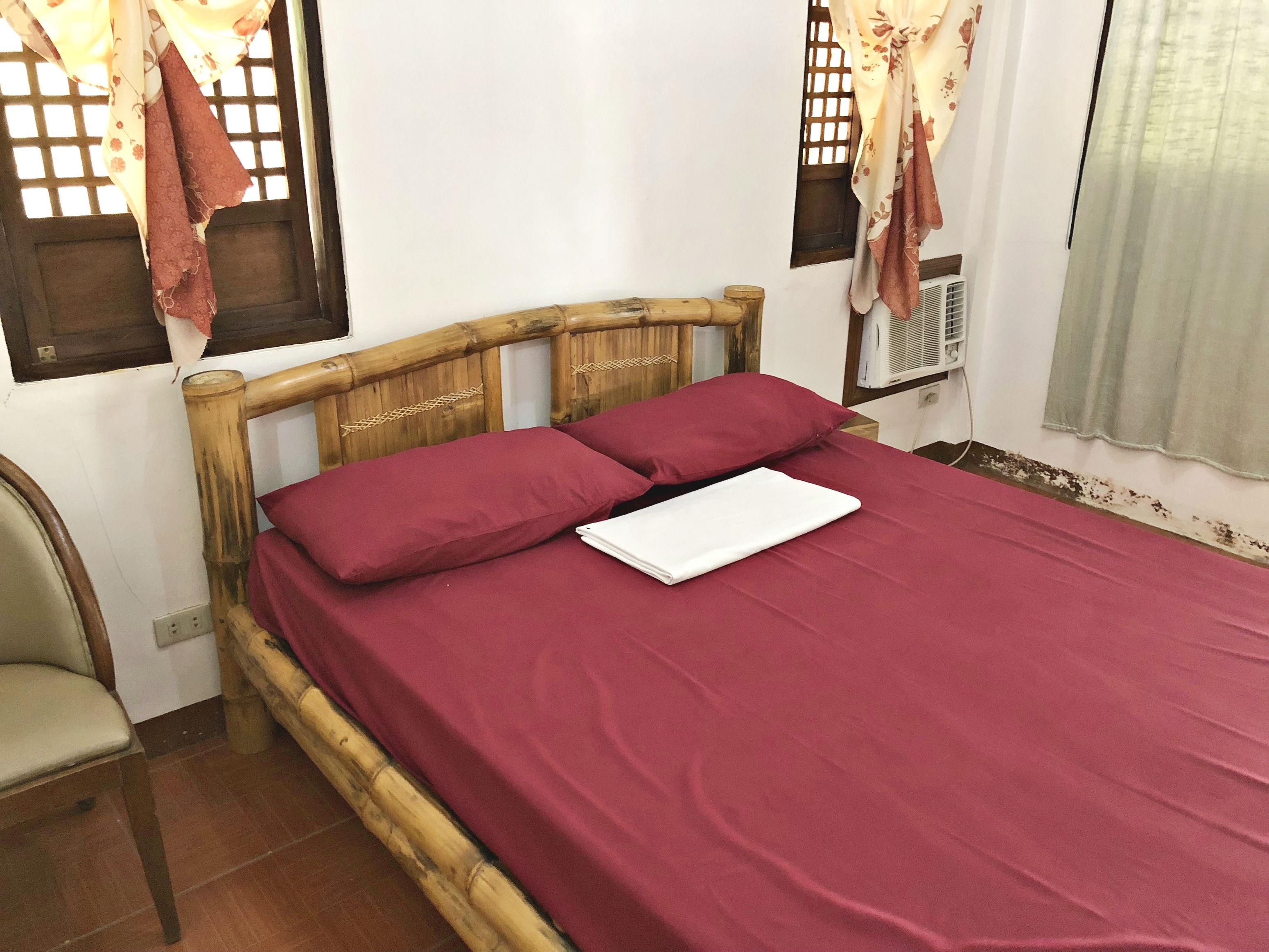 A bed with a wooden headboard, a red bedspread, and two pillows.