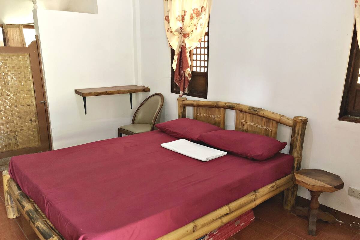A bed with a red bedspread, a wooden headboard, and a wooden nightstand with a lamp.