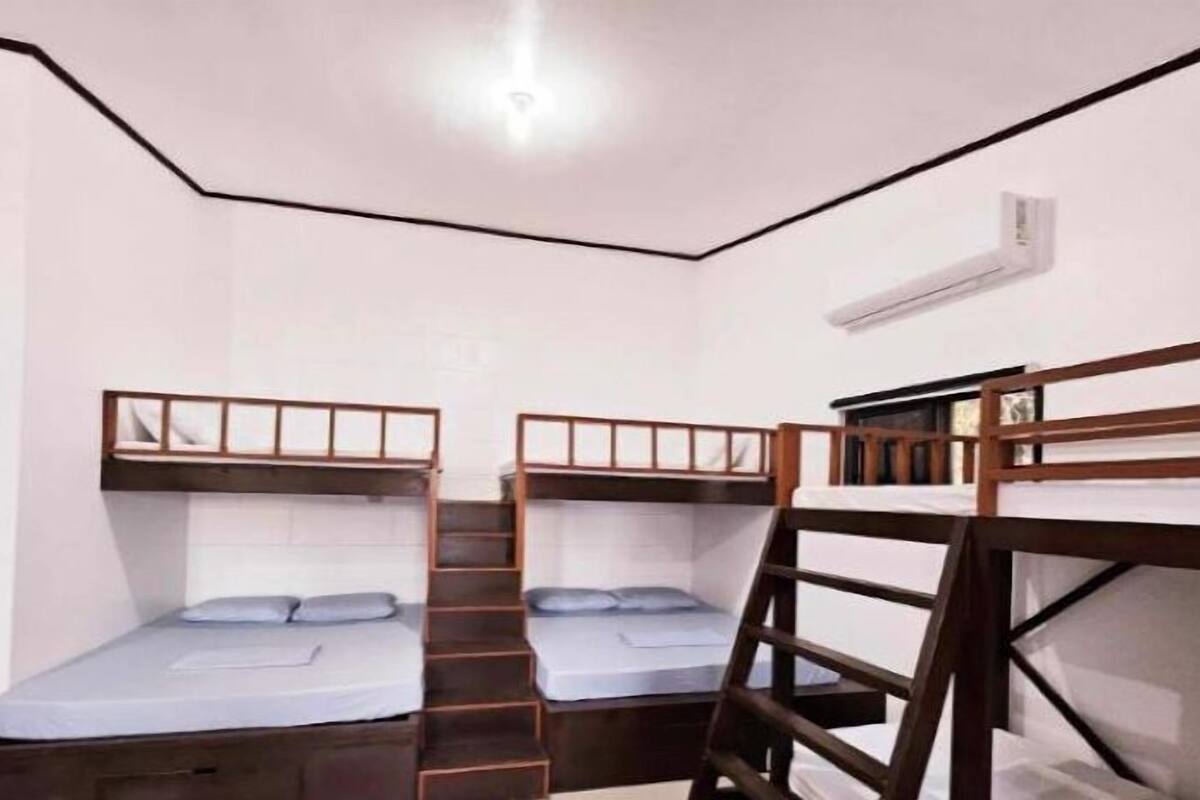 A small, compact room with bunk beds, a wooden ladder, and a white wall with a window.