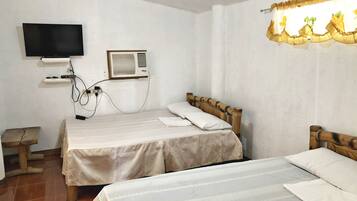 Una habitación con dos camas, un televisor montado en la pared y una ventana con cortina.
