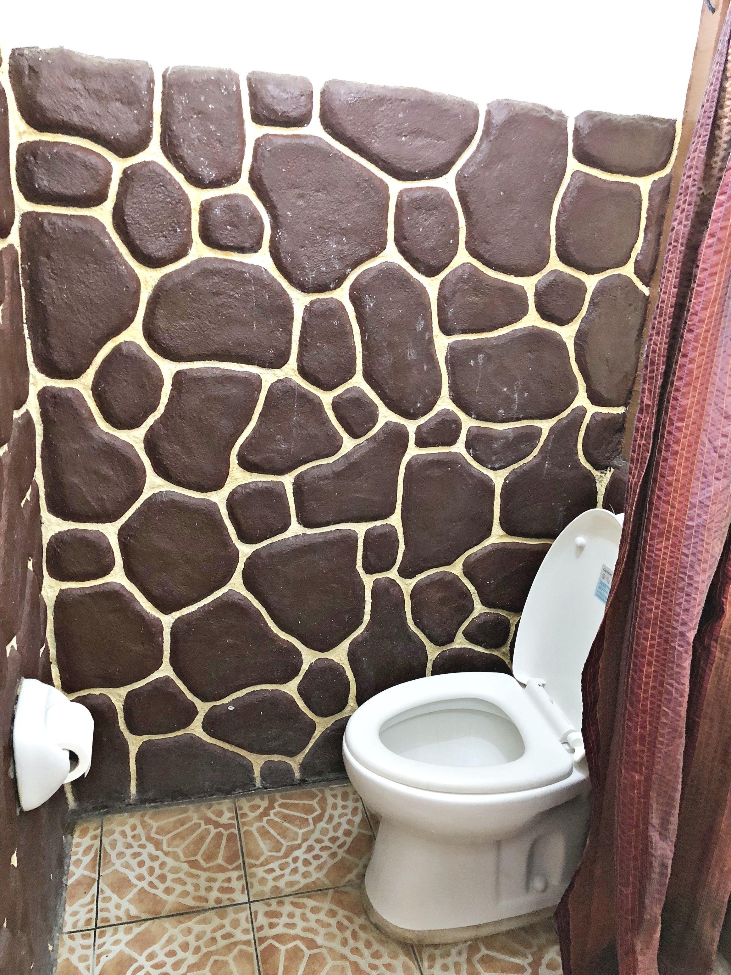 Un baño con pared de piedra, inodoro y baldosas de suelo con diseño.