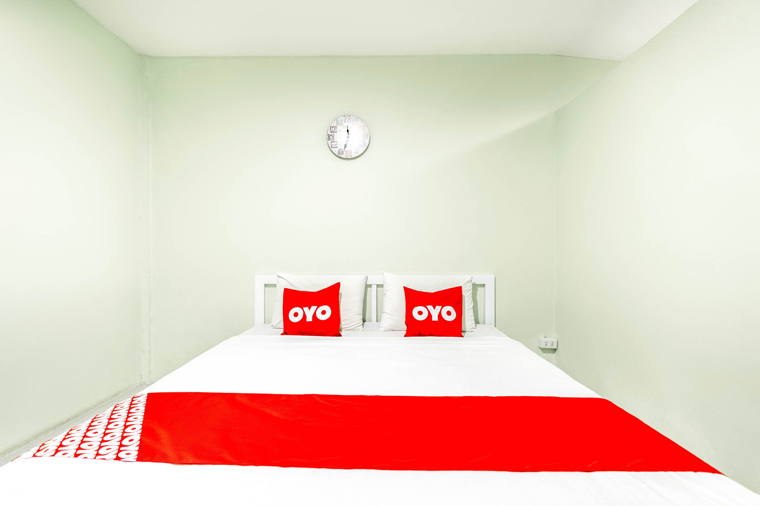 Une chambre avec un lit, deux oreillers ornés du texte « OYO », une tête de lit blanche et une horloge murale.