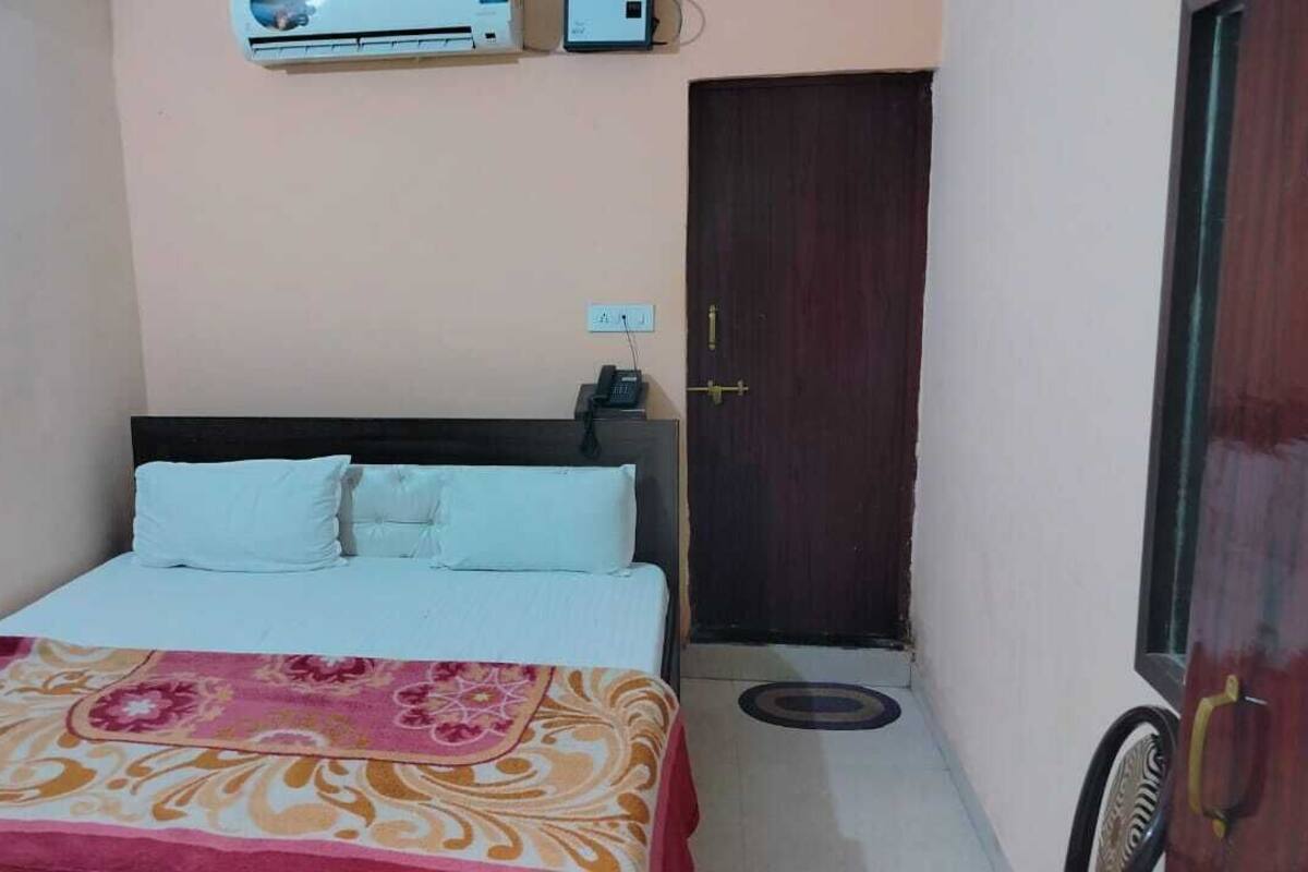 A small, neatly arranged bedroom with a bed, a bedside table, a wall-mounted air conditioner, and a door.