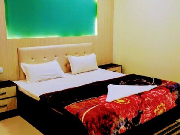 A hotel room with a bed, a nightstand, and a wall-mounted light fixture. - Hotel Utsav Residency (Varanasi)