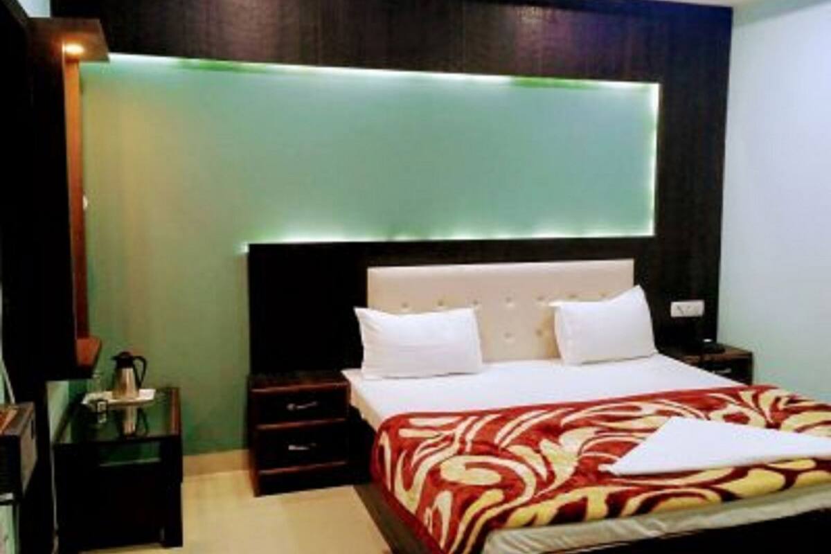 A hotel room with a bed, bedside tables, a nightstand, and a wall-mounted light fixture.