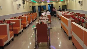 Un restaurante con filas de asientos anaranjados, una araña y luces de techo.