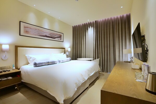 A hotel room with a large bed, bedside tables, a desk, and a TV.