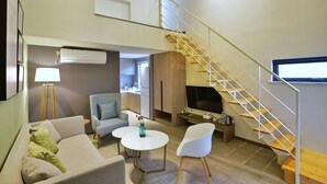 A modern living room with a sofa, two chairs, a coffee table, a TV, and a staircase.