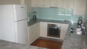 Una cocina compacta con refrigerador, horno, pileta y licuadora sobre la encimera.
