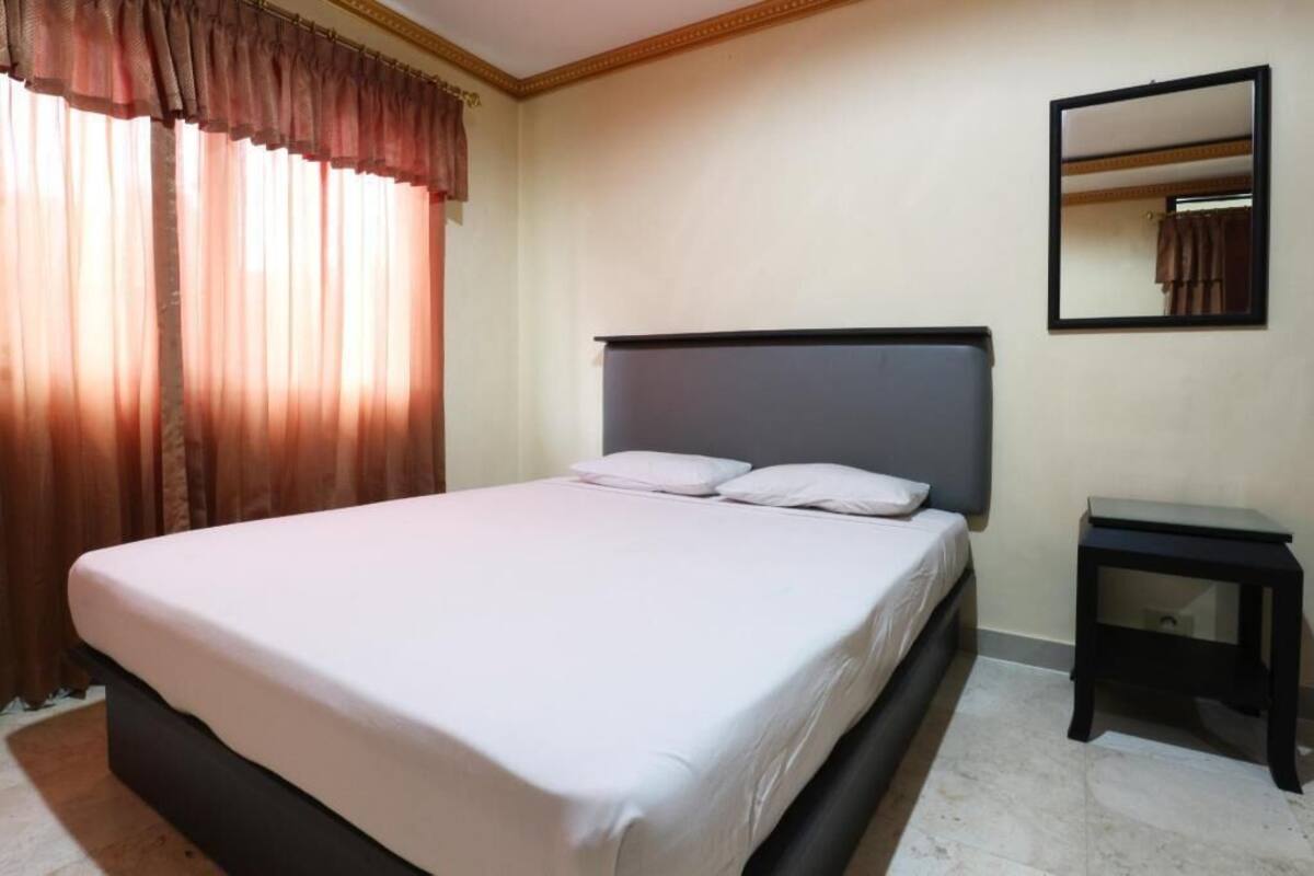 Una habitación de hotel con una cama, una mesita de noche, un espejo y cortinas.
