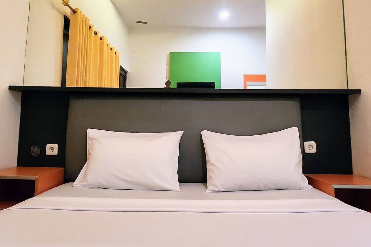 Habitación de hotel con una cama, dos almohadas, un cabecero y una mesita de noche a cada lado.