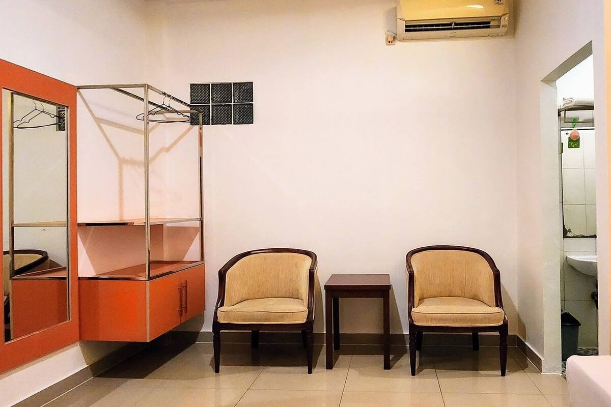 Una habitación con armario, dos sillas, una mesita, un espejo y aire acondicionado instalado en la pared.