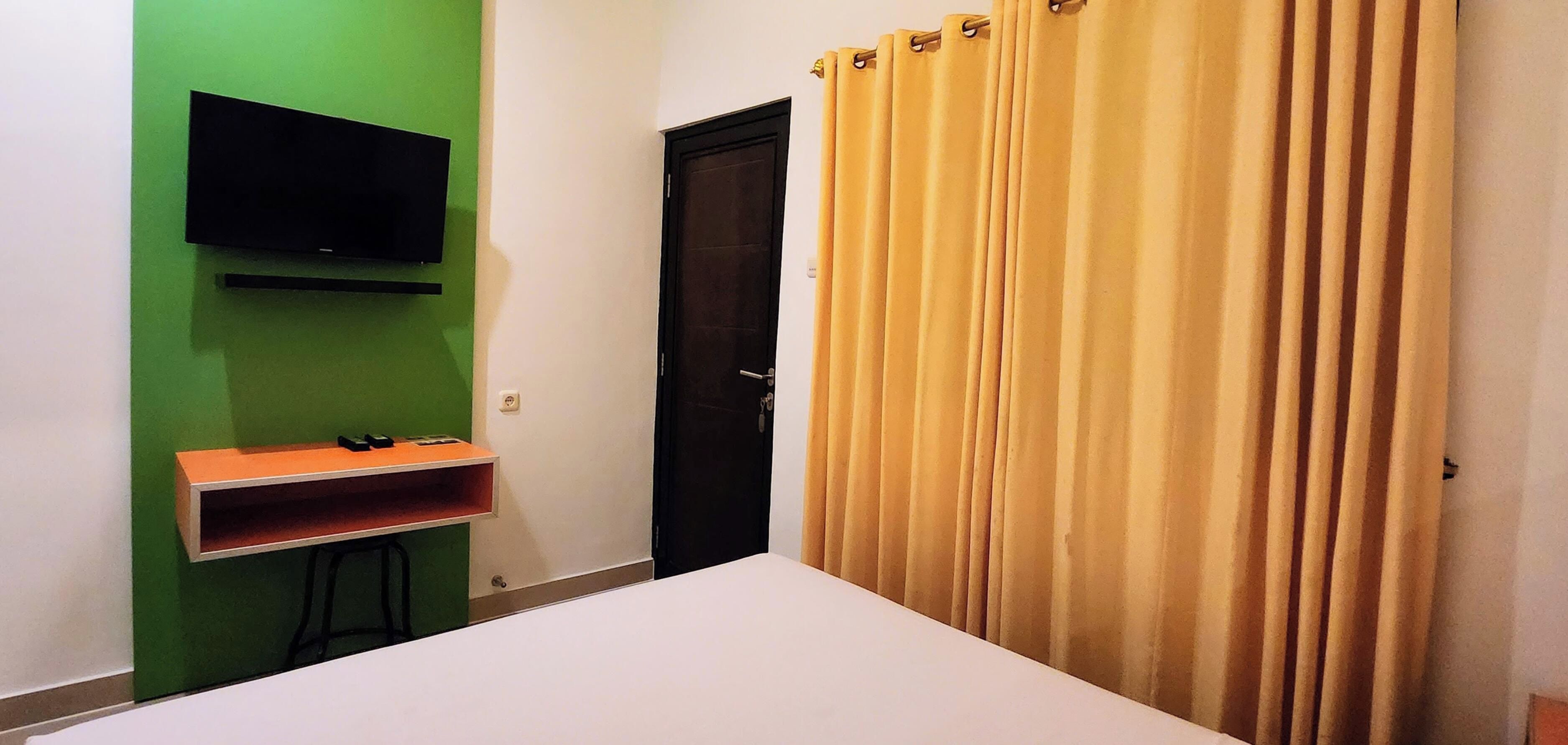 Una habitación con una cama, un televisor instalado en una pared verde, una puerta y una cortina.