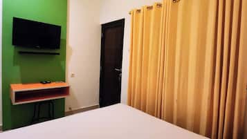 A room with a bed, a TV mounted on a green wall, a door, and a curtain.