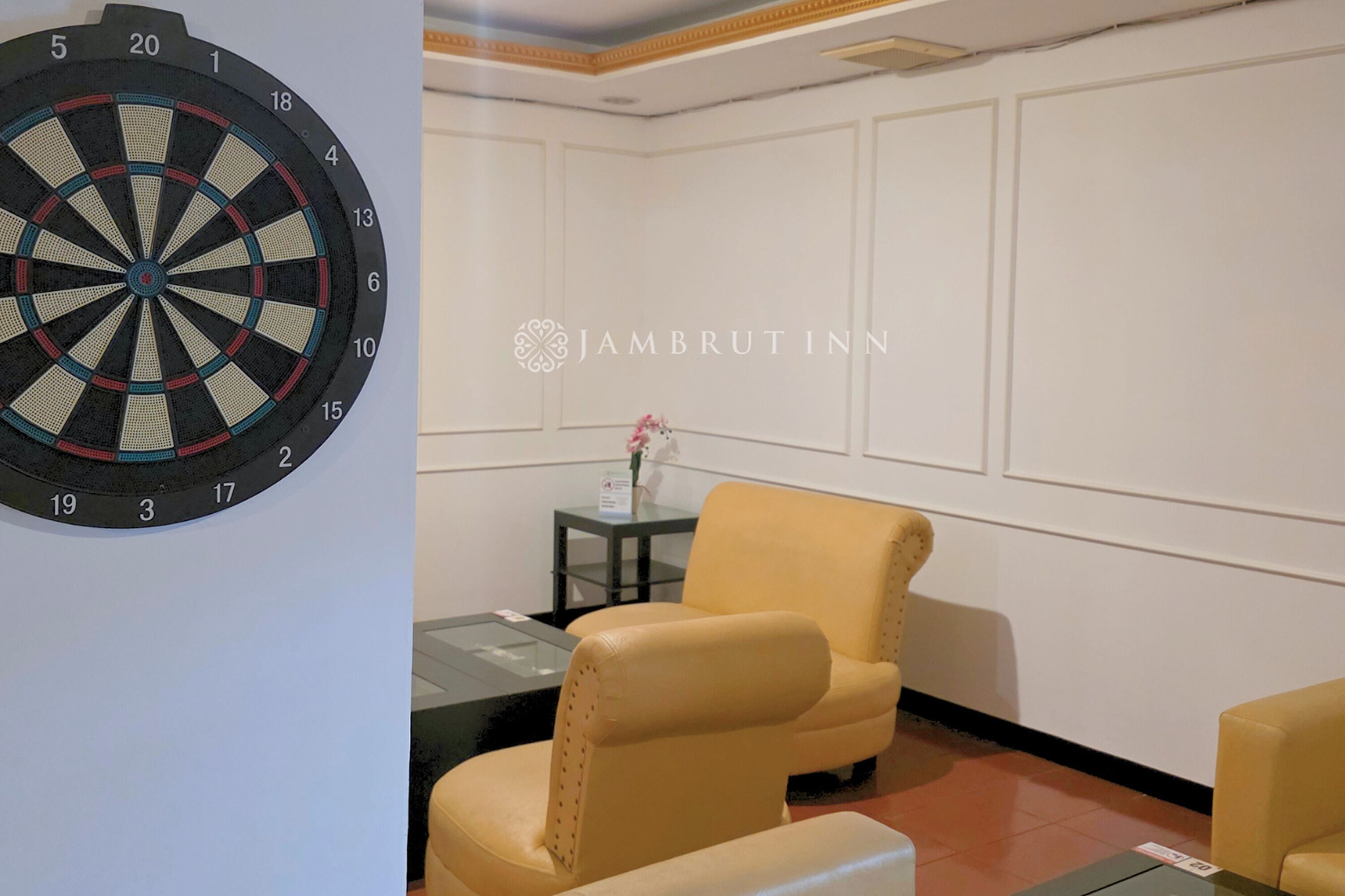 Un jeu de fléchettes et une pièce avec un fauteuil jaune et une petite table sur laquelle se trouve un vase.
