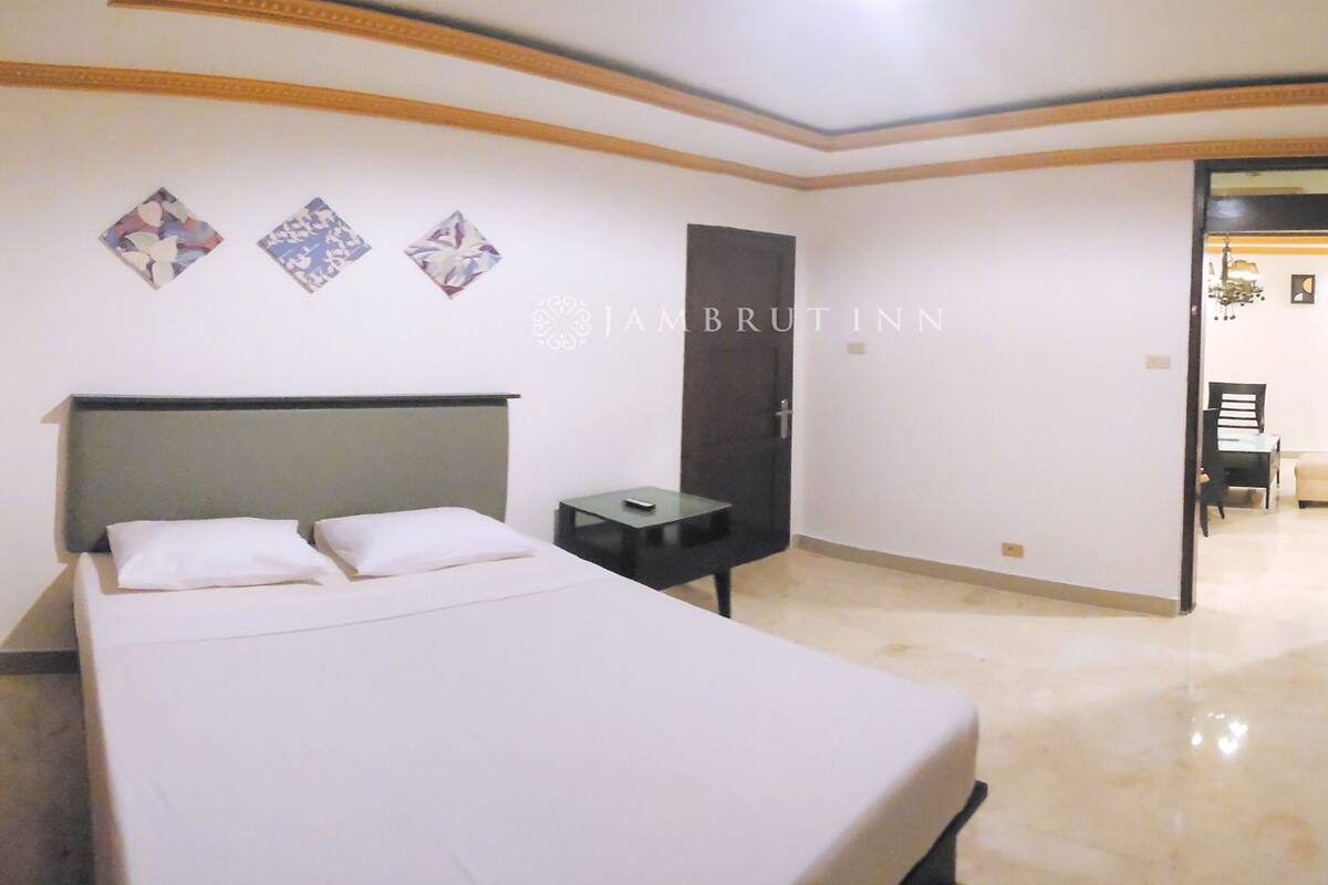 Una habitación de hotel con una cama grande, una mesita de noche, una puerta y una pequeña mesa.