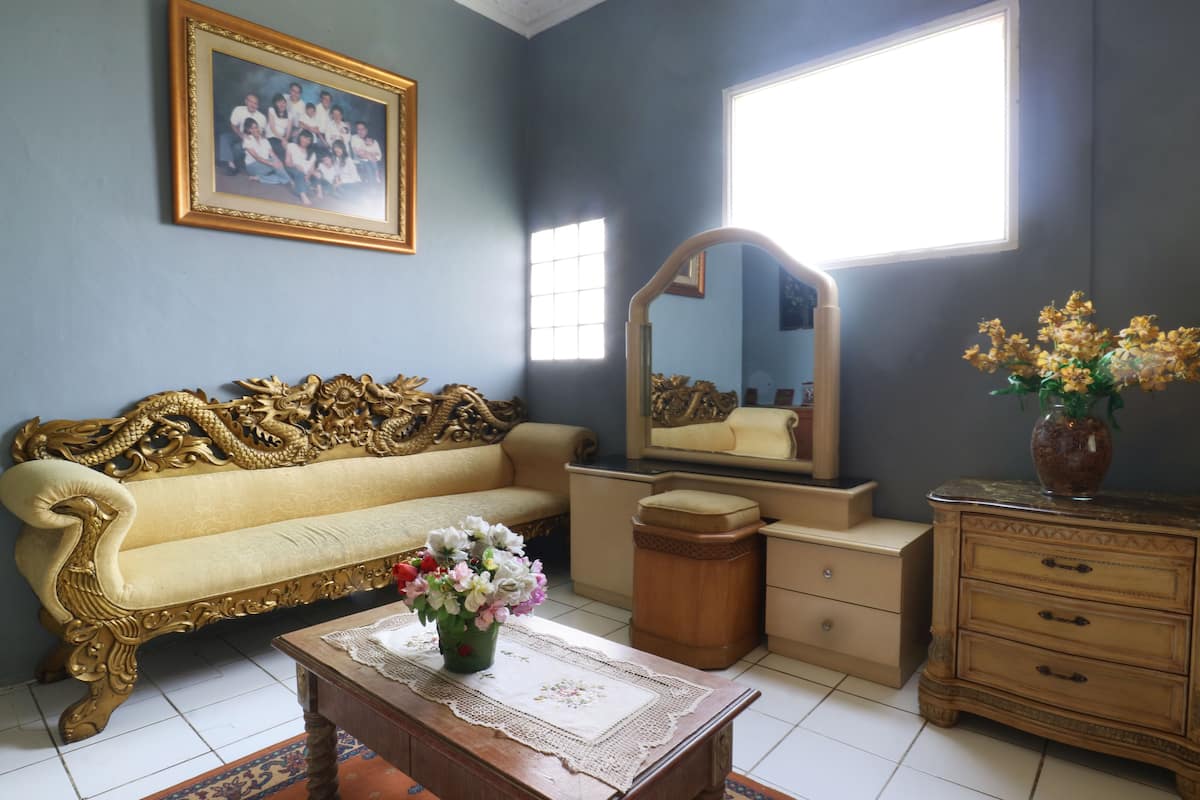 Ein Zimmer mit einer Couch, einem Couchtisch mit Blumen, einem Schminktisch, einem Spiegel und einem gerahmten Bild an der Wand.