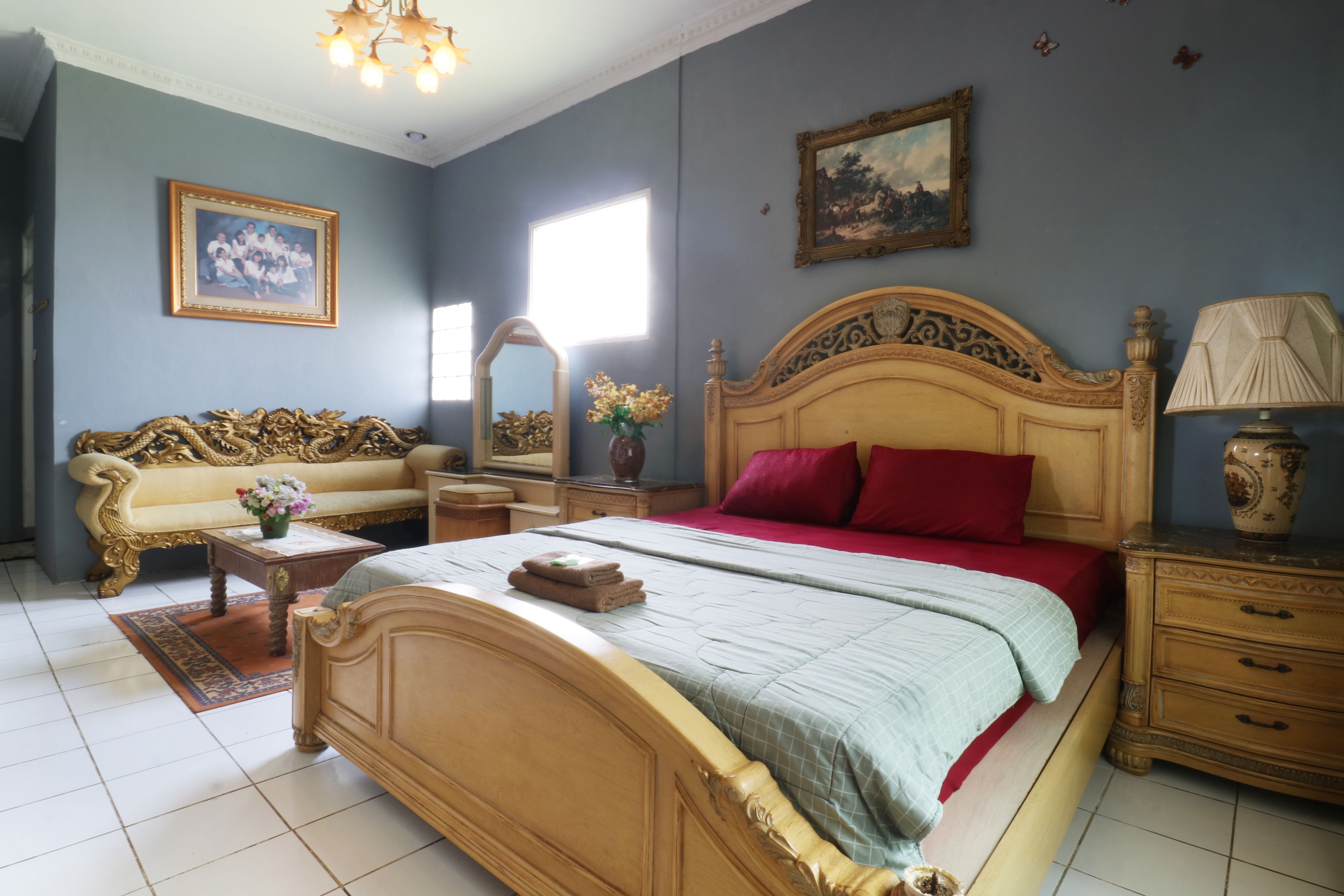 A bedroom with a large bed, a sofa, a nightstand, a lamp, and a mirror.