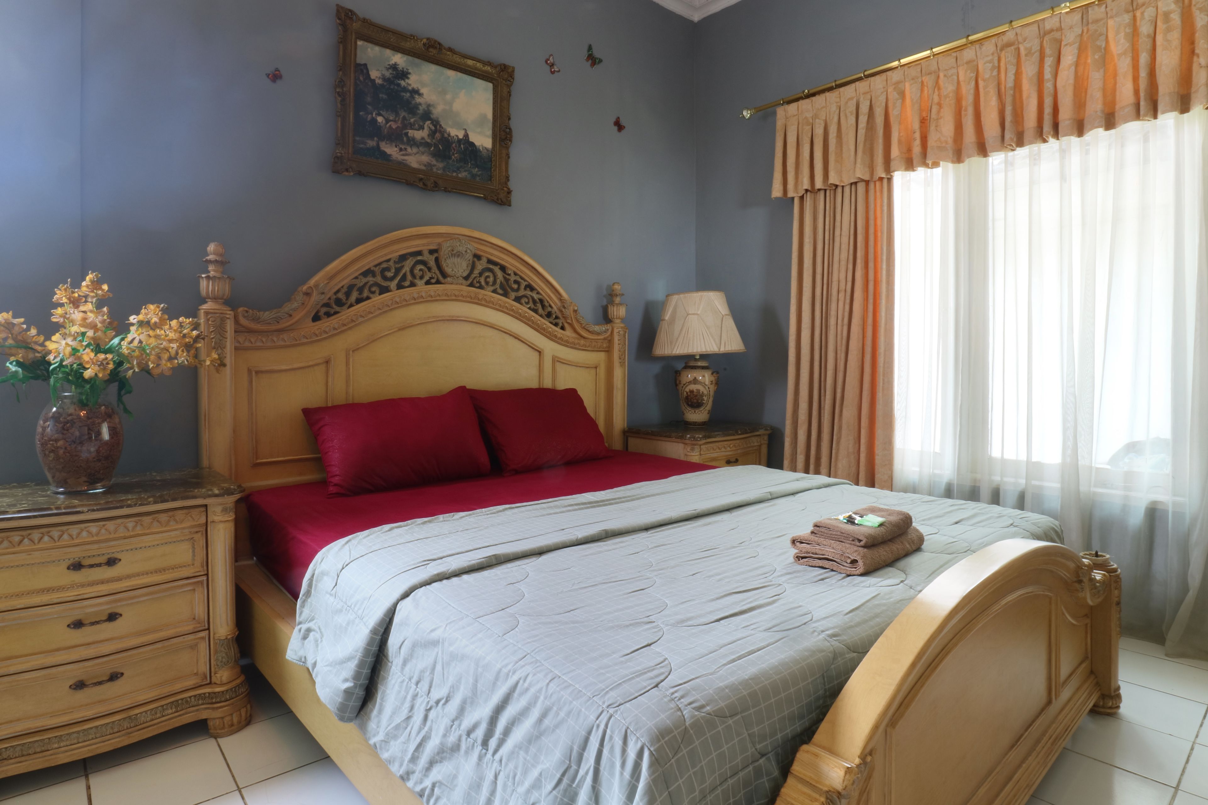 Une chambre à coucher avec un grand lit, une table de chevet avec une lampe, un vase de fleurs et un tableau accroché au mur.