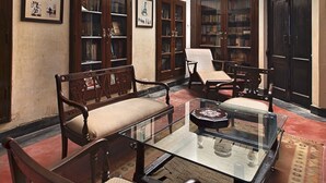 Una habitación amplia con techo alto, ventilador de techo y una mesa de centro de vidrio rodeada de sillas de madera.