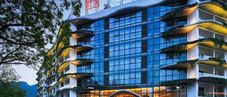 Ein modernes Hotel mit einer geschwungenen Fassade, mehreren begrünten Balkonen und freiem Blick auf die umliegende Landschaft.