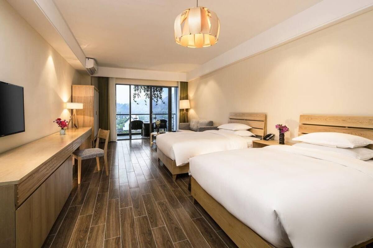Habitación de hotel con dos camas, un escritorio, un televisor de pantalla plana, una silla y un amplio ventanal con vistas al exterior.