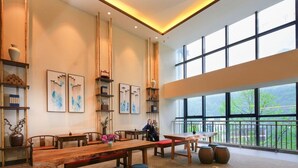 Un comedor amplio con mesas y sillas de madera, ventanas grandes con vistas y estanterías con objetos decorativos.