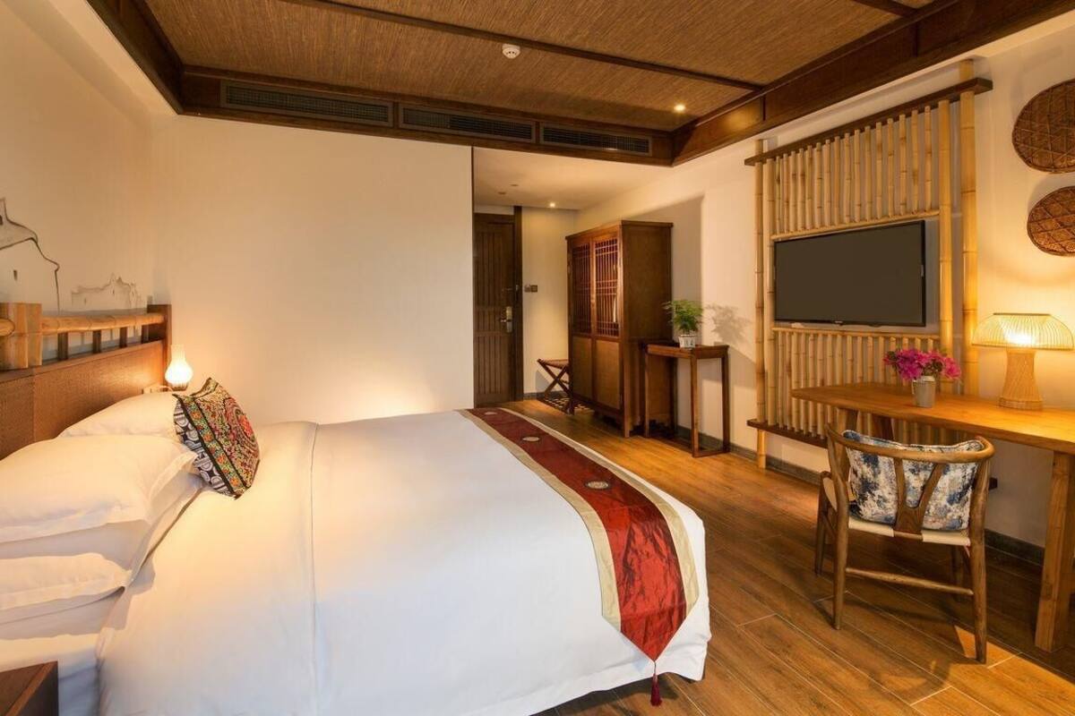 Habitación de hotel con cama, escritorio, silla, televisor y una pequeña mesa con planta.