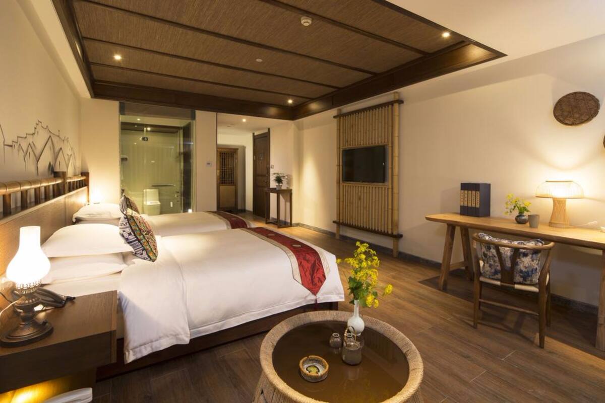 Habitación de hotel con cama, mesita de noche, lámpara y una pequeña mesa con un florero.