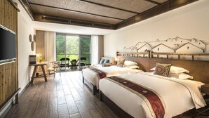 Habitación de hotel con dos camas, un ventanal con vistas a la vegetación, un televisor de pantalla plana y una obra de arte colgada en la pared que representa montañas.