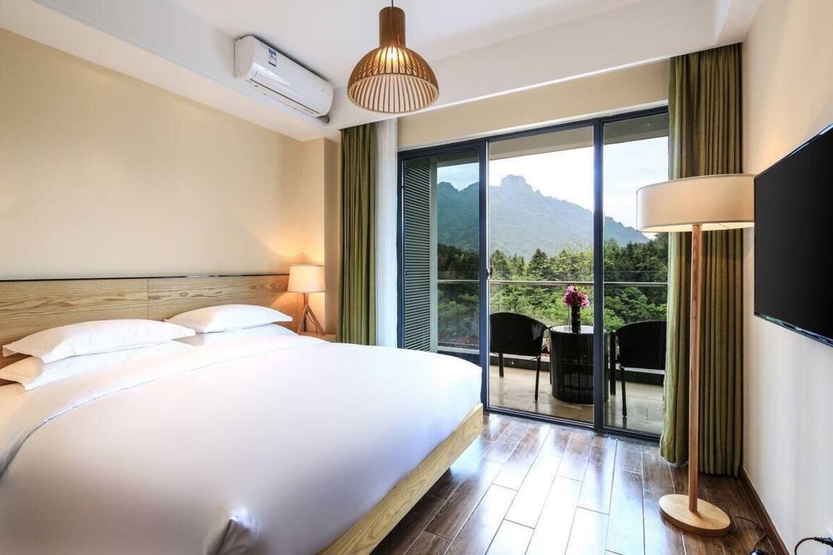 Habitación de hotel con una cama grande, un televisor de pantalla plana, un ventilador de techo y un balcón con vistas a las montañas.