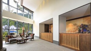 Un hall amplio con mostrador de recepción, zona de estar y ventanas grandes que ofrecen vistas a zonas verdes.