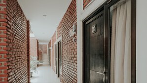 Un couloir aux murs de briques, au sol carrelé, et une porte portant un numéro.