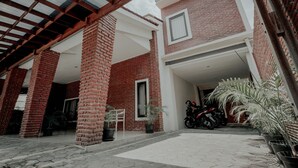 Un espace extérieur abrité, doté de murs en briques, d’une moto, de plantes en pot et d’une chaise.