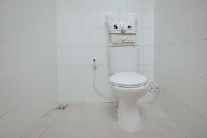 A white toilet with a basket of towels on top, a visible water pipe, and a tiled floor. - D'Paragon Cherry (Depok)