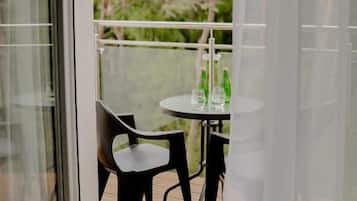Un balcón con mesa y sillas, un vidrio y vista a árboles.