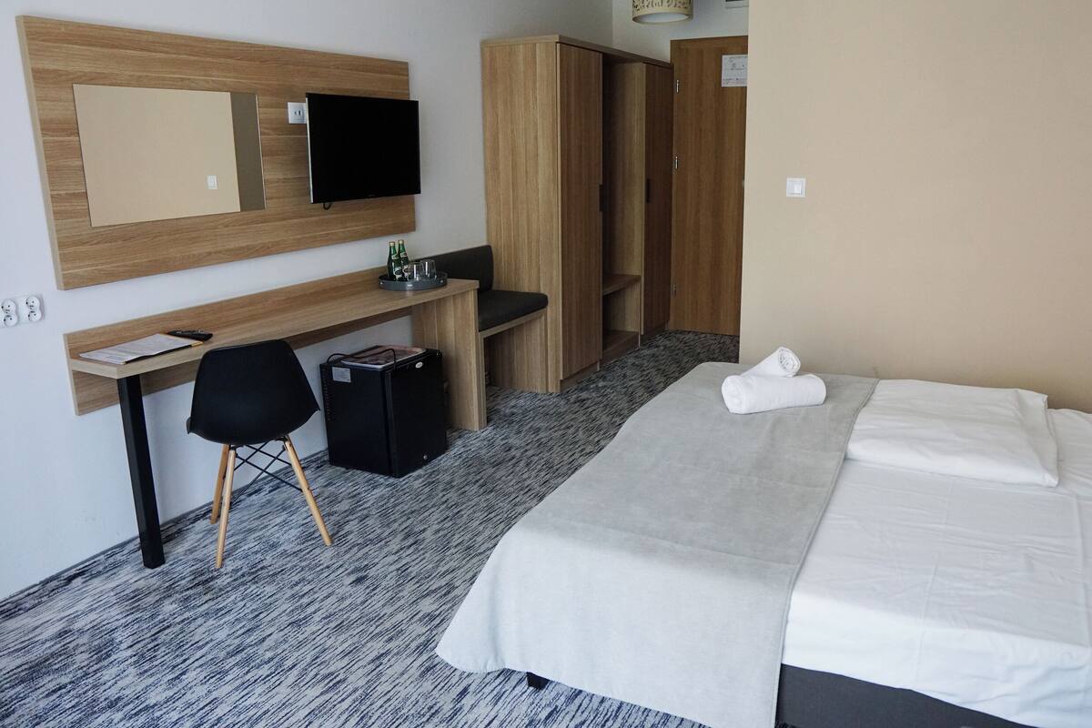 Quarto de hotel com cama, escrivaninha, cadeira, guarda-roupa e televisão.