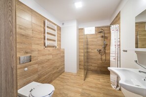 A modern bathroom with a wooden wall, a white toilet, a shower with a glass door, and a white sink. - Wydma Resort (Trzebiatow)