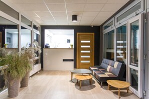 A modern interior with a reception desk, a wooden door, a sofa, and two small tables. - Wydma Resort (Trzebiatow)