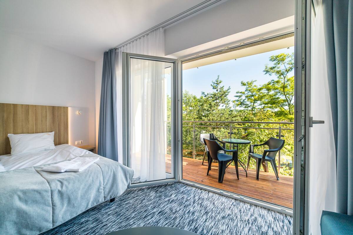 Quarto de hotel com cama, uma mesa pequena e varanda com cadeiras.