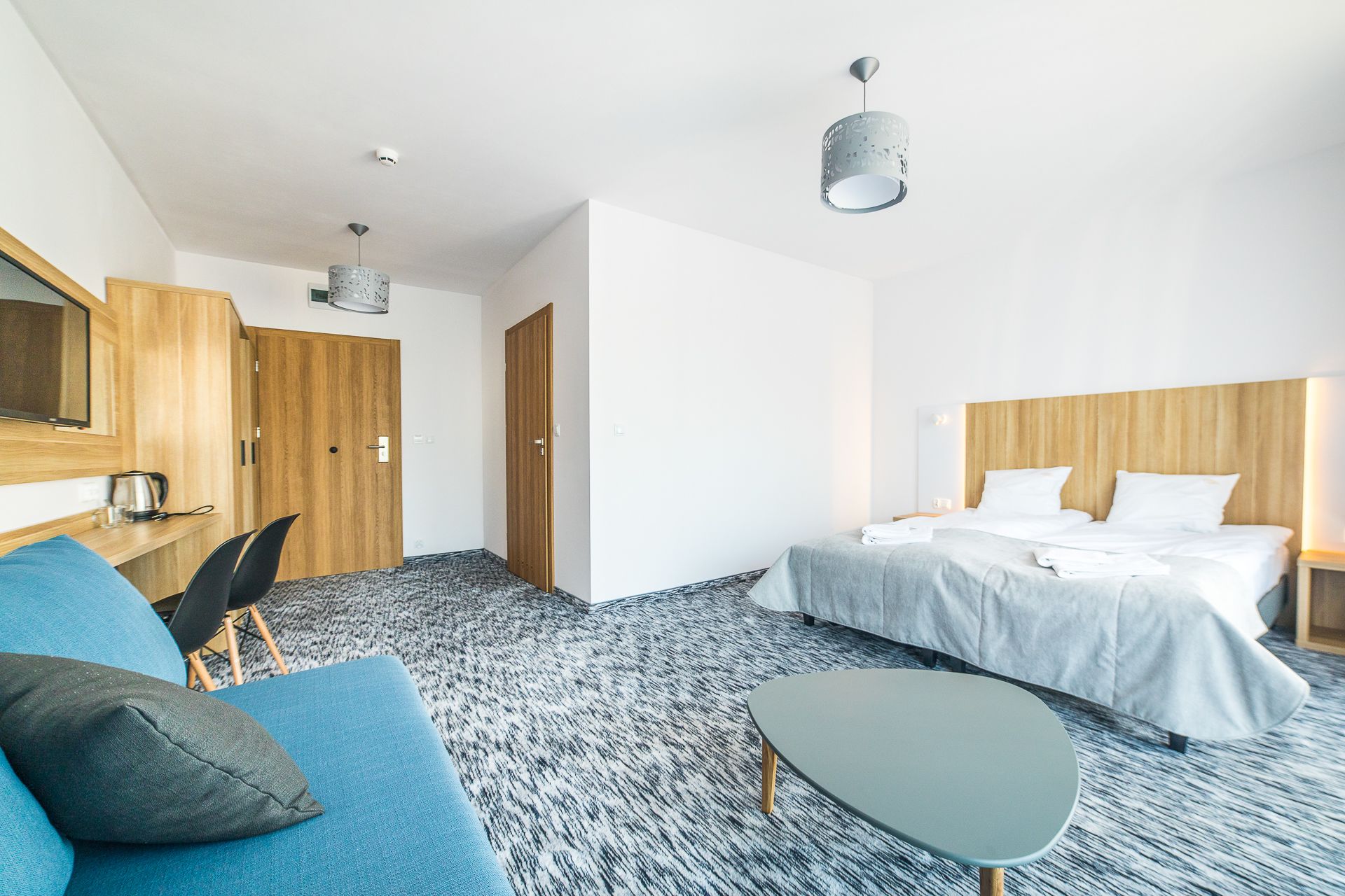 A modern hotel room with a bed, a sofa, a small table, and a desk with a chair.