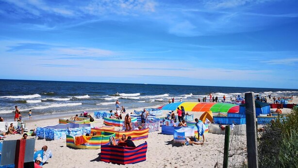 A beach with colorful umbrellas and beach chairs, a wooden fence, and the ocean in the background. - Wydma Resort (Trzebiatow)