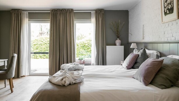 Une chambre à coucher avec un lit, une chaise, un radiateur et une fenêtre avec des rideaux.