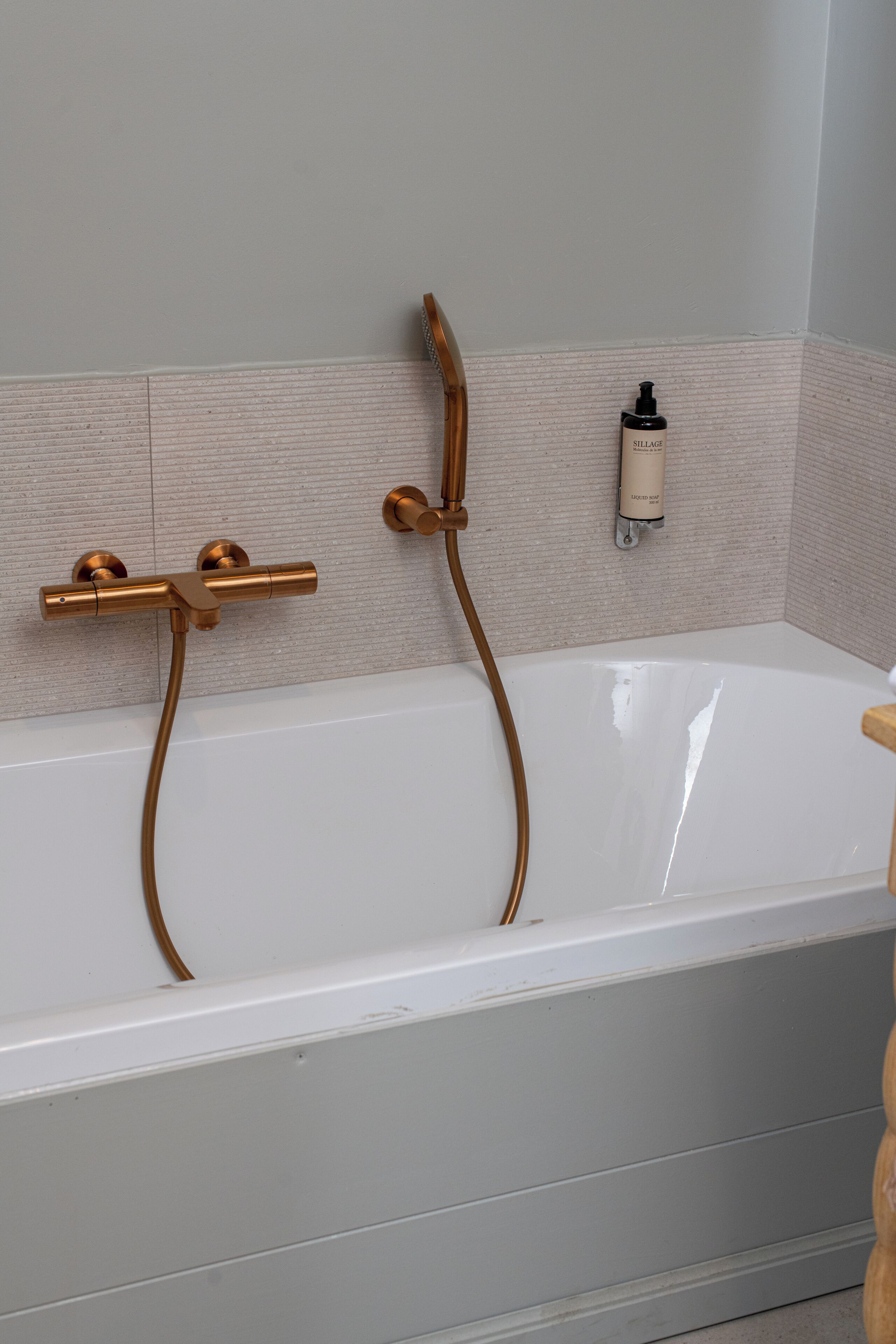 Une salle de bain moderne avec une baignoire blanche, des accessoires en cuivre et un distributeur de savon fixé au mur.
