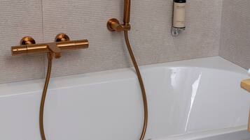 Une salle de bain moderne avec une baignoire blanche, des accessoires en cuivre et un distributeur de savon fixé au mur.