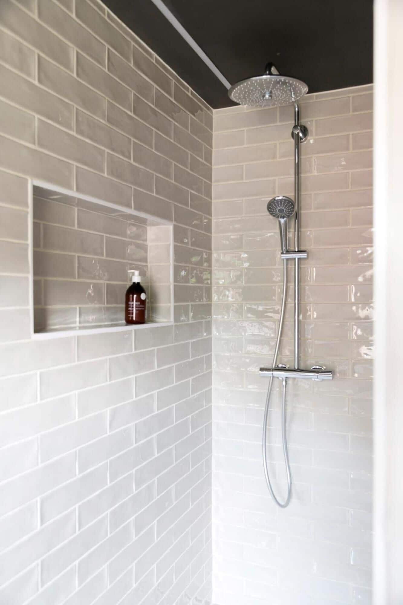 A shower with a handheld showerhead and a wall-mounted faucet, set against a white brick wall.