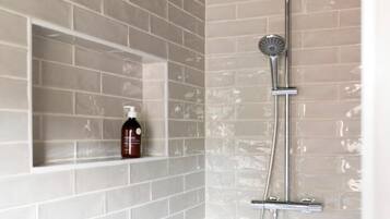 A shower with a handheld showerhead and a wall-mounted faucet, set against a white brick wall.