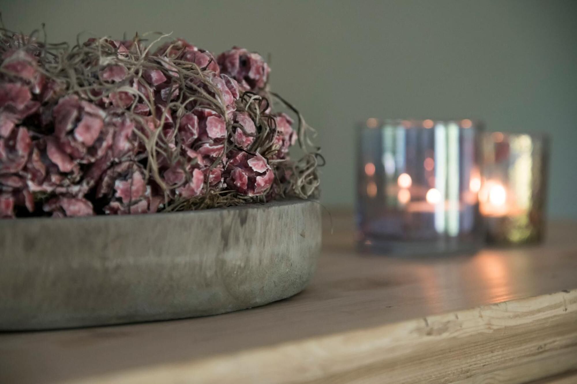 Ein Holztisch mit einer Schale getrockneter Blumen und zwei brennenden Kerzen.