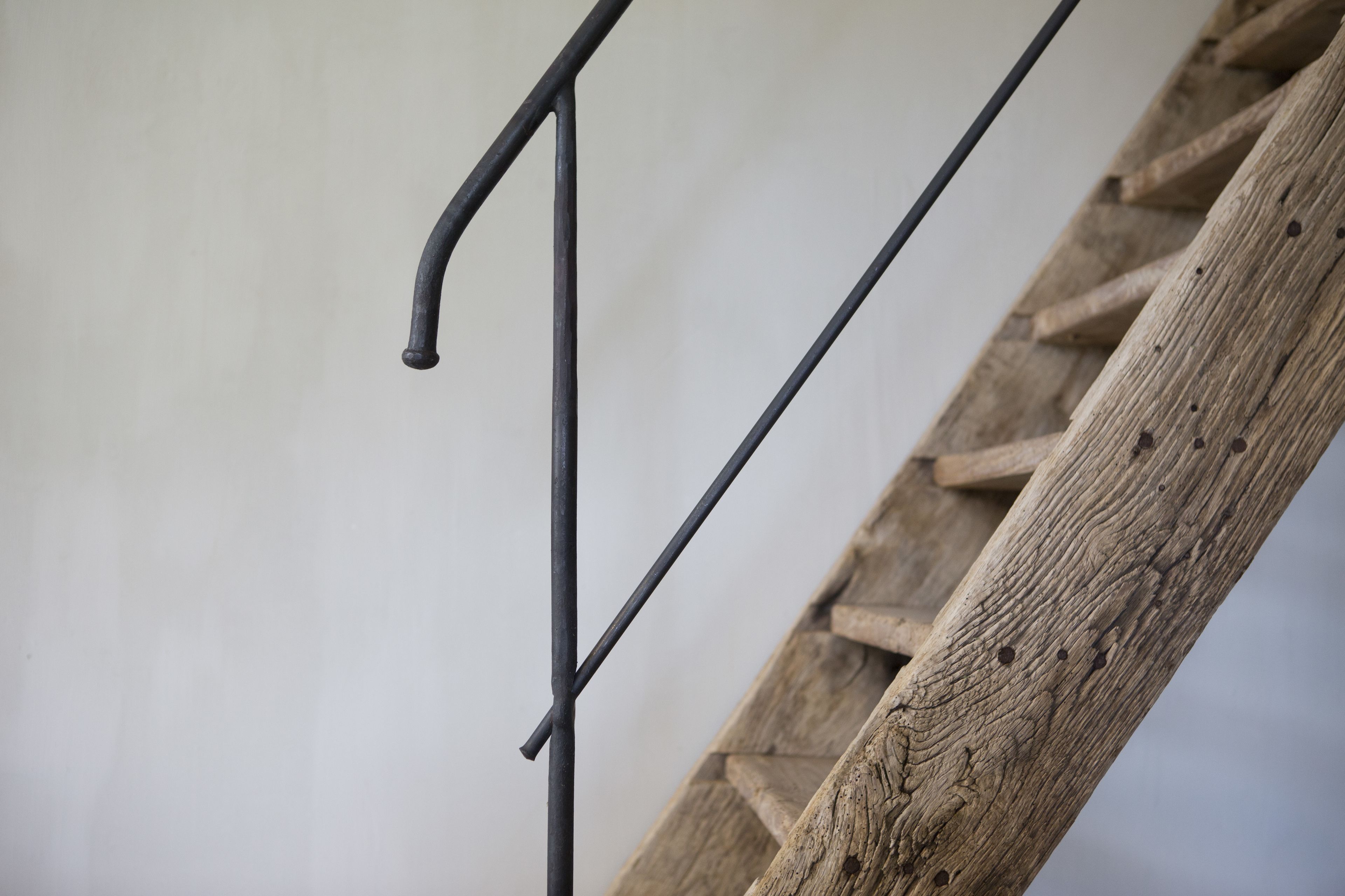Una escalera de madera con peldaños metálicos apoyada en una pared lisa.