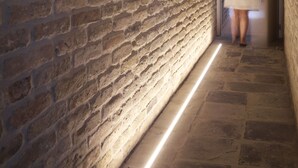 Un couloir avec un mur en briques et une bande lumineuse au sol.